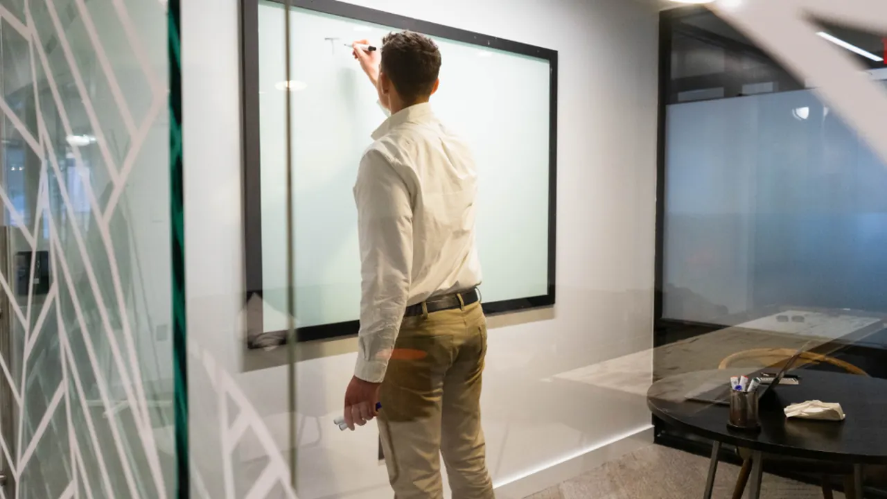 A man writing a strategy on a glass whiteboard in a modern office
