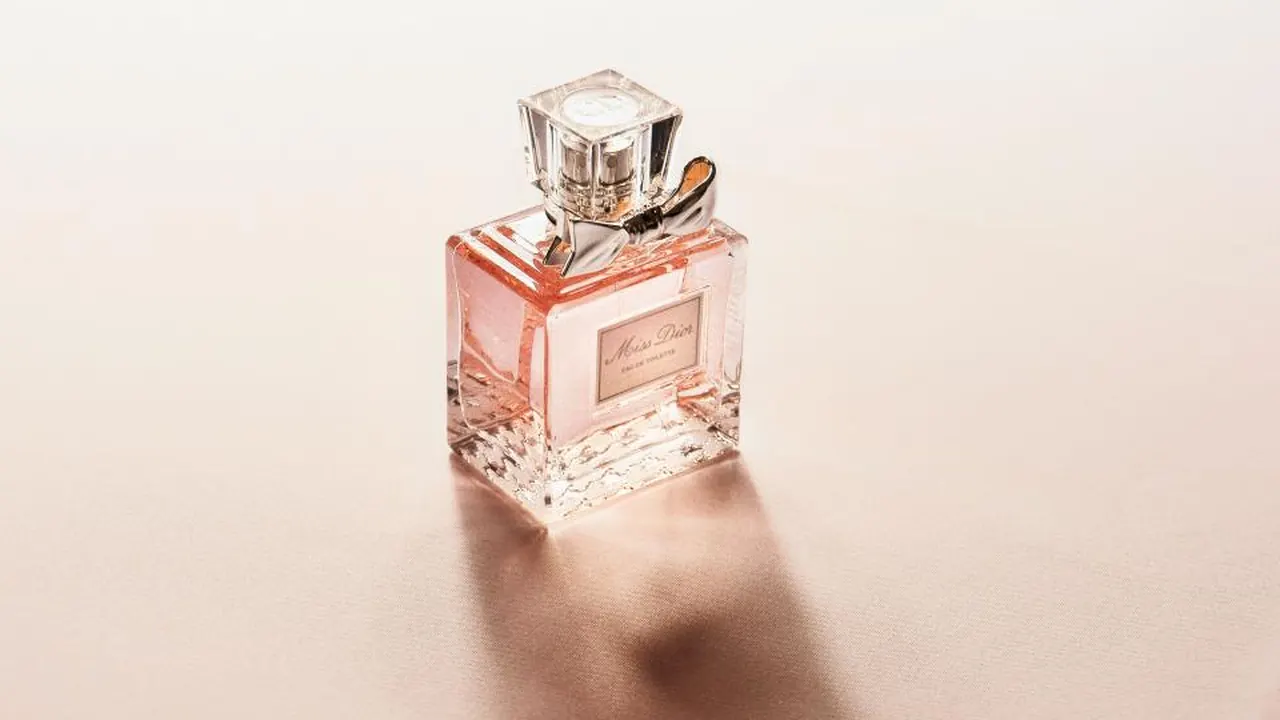 A pink glass perfume bottle on a soft cream background