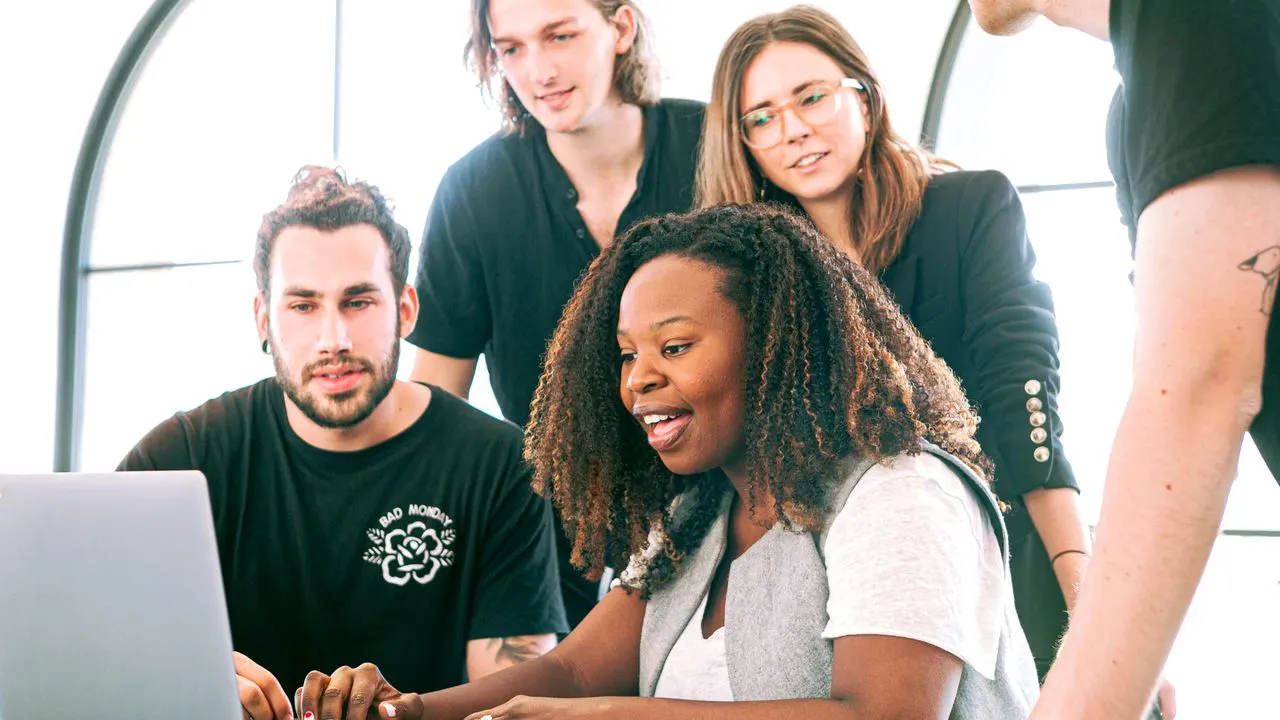 A group of new learners gathered around a laptop, smiling