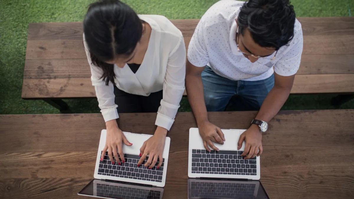 Two coworkers working side by side on laptops at a table