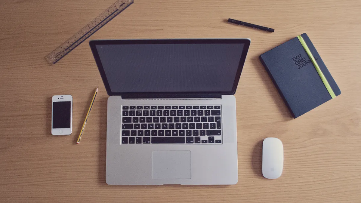 A laptop, notebook and phone arranged on a wooden desk