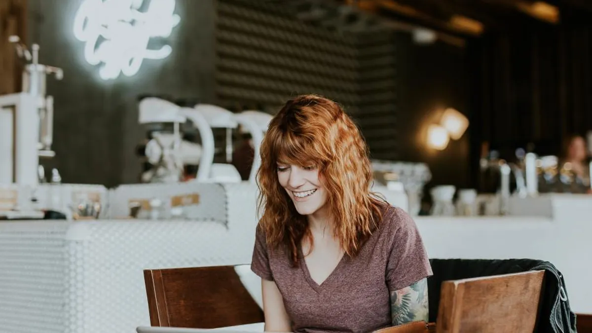 A smiling woman working on a laptop in a cafe