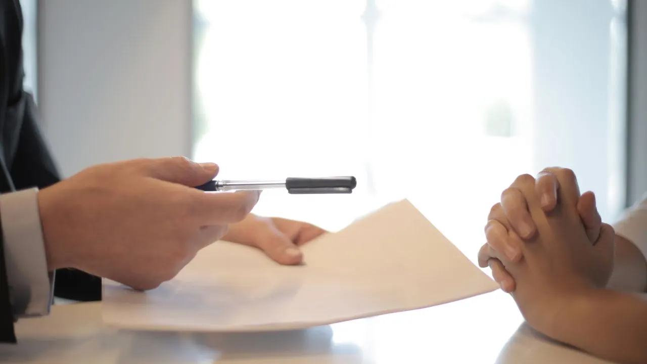 An offer document and pen being handed across a desk