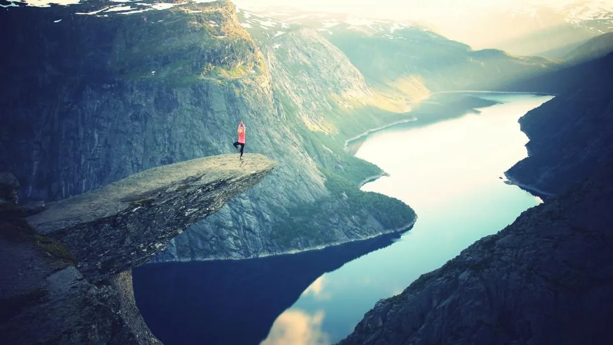 A person standing on a cliff edge overlooking a mountain fjord