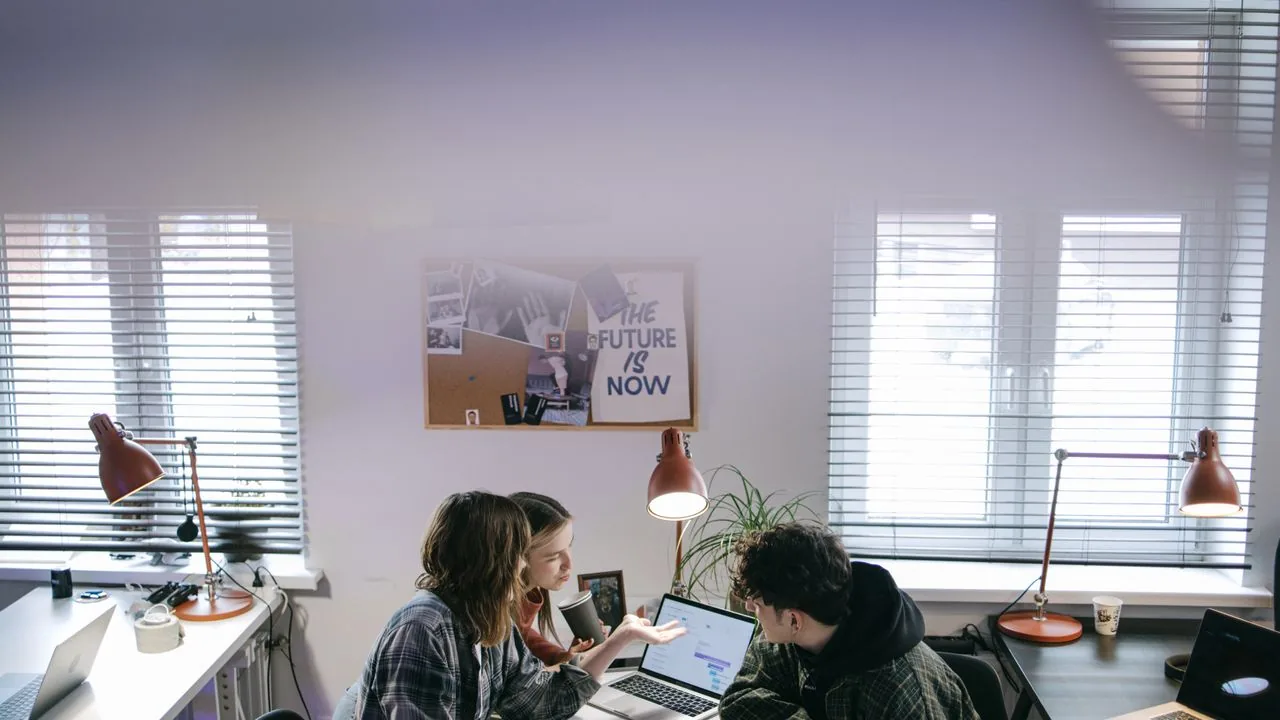 Young professionals working at laptops beneath a poster reading "The Future Is Now"