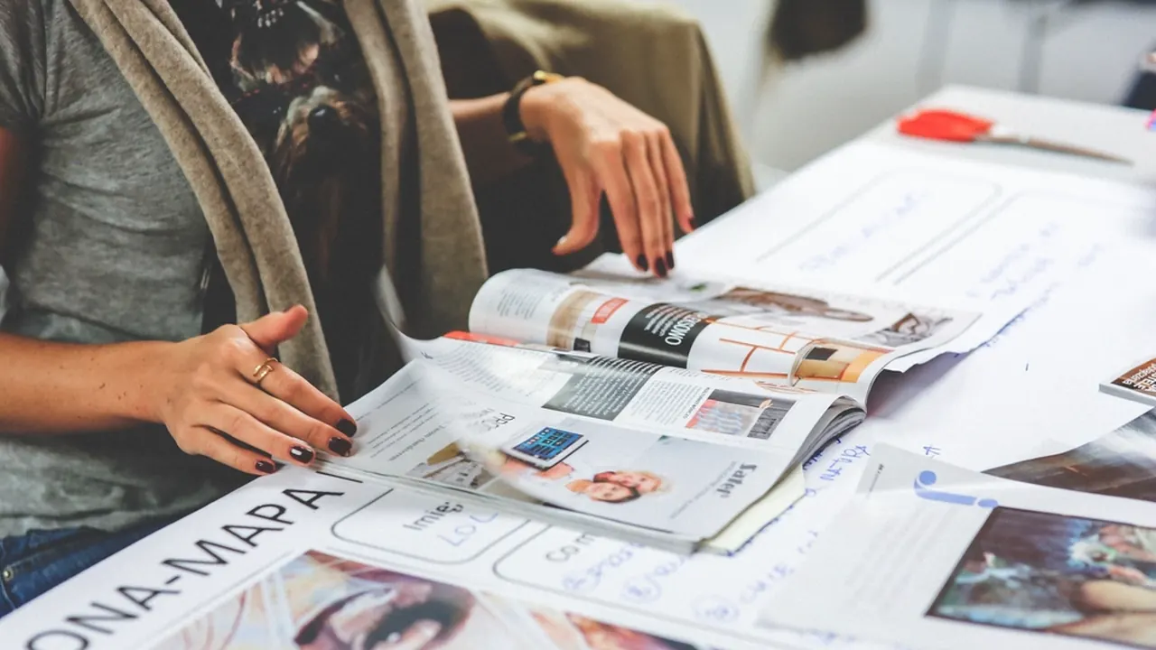 A person reading fashion magazines spread across a table
