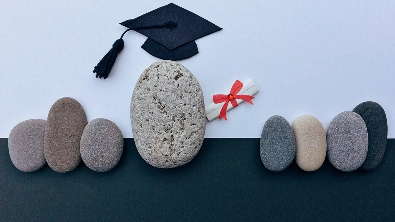A graduation cap resting on a large stone beside a rolled certificate