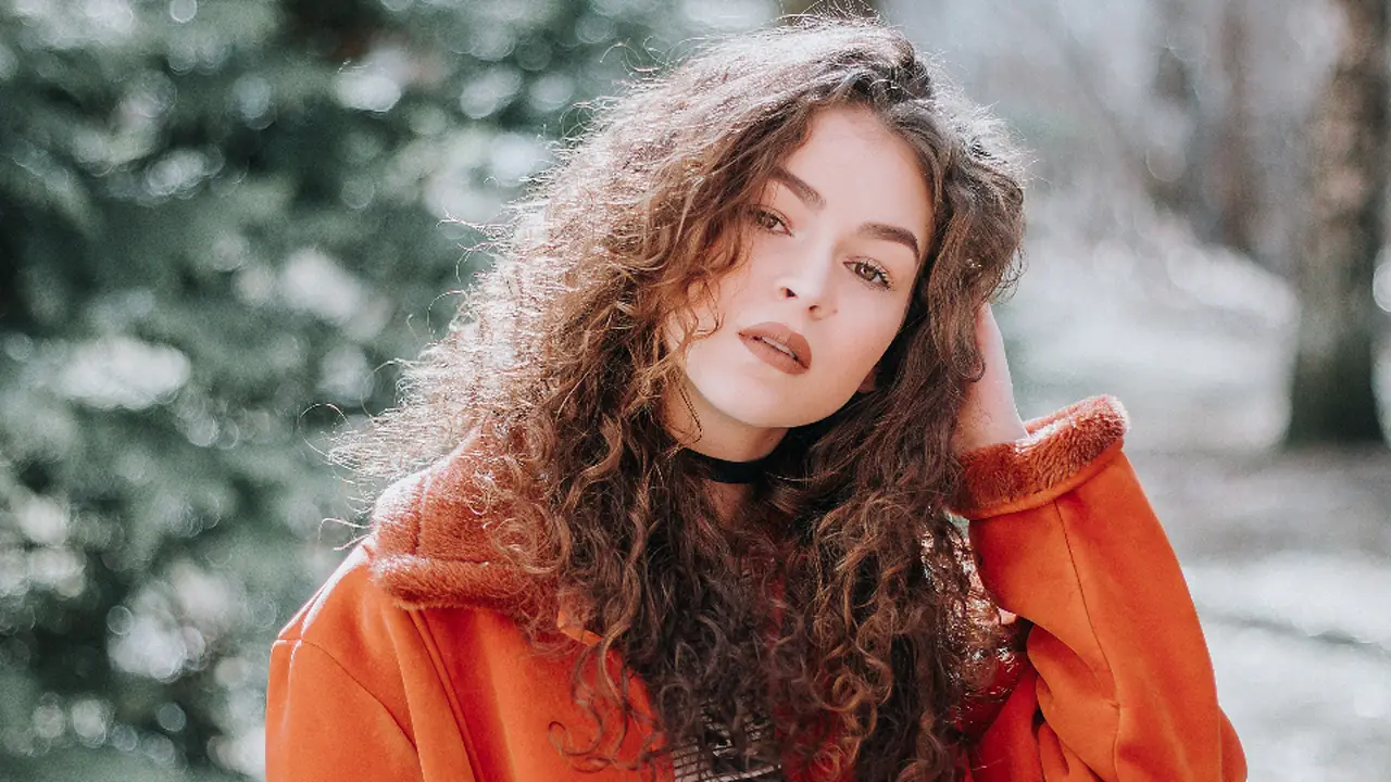 A fashion portrait of a woman with curly hair in an orange coat