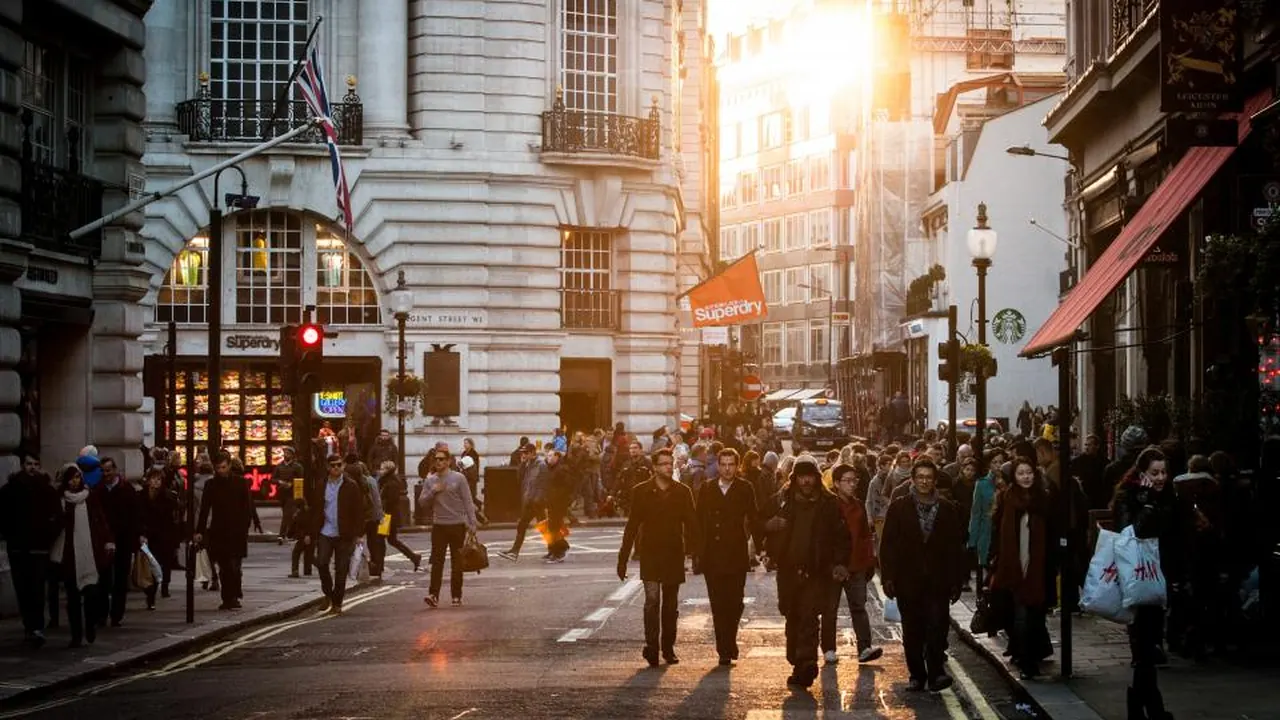Shoppers walking down a London street lined with historic buildings at sunset