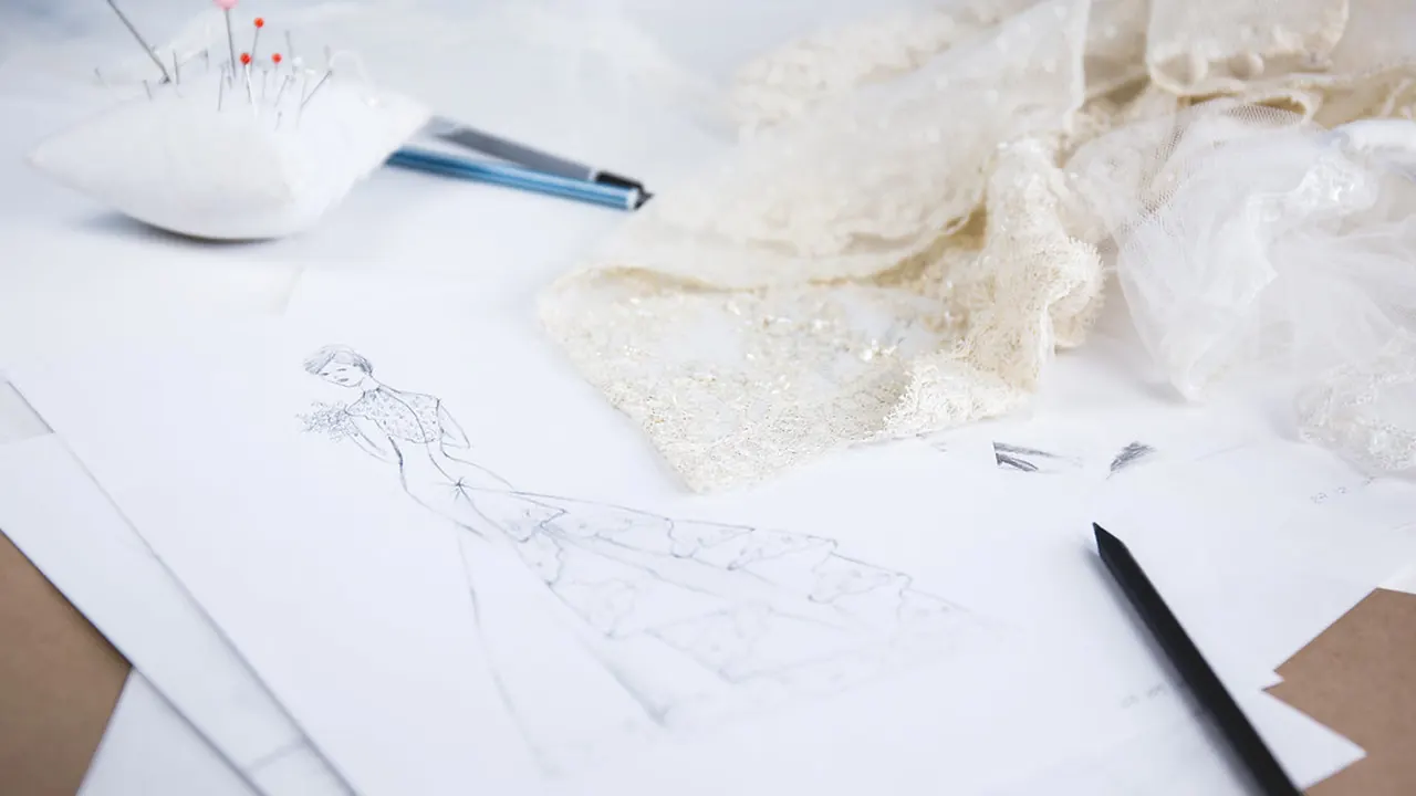 Fashion design sketches and pencils spread across a white worktable