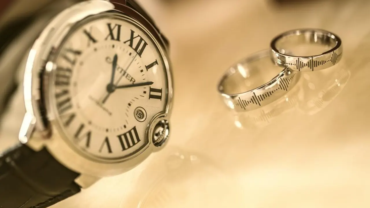 A classic luxury wristwatch beside two rings on a warm-toned surface