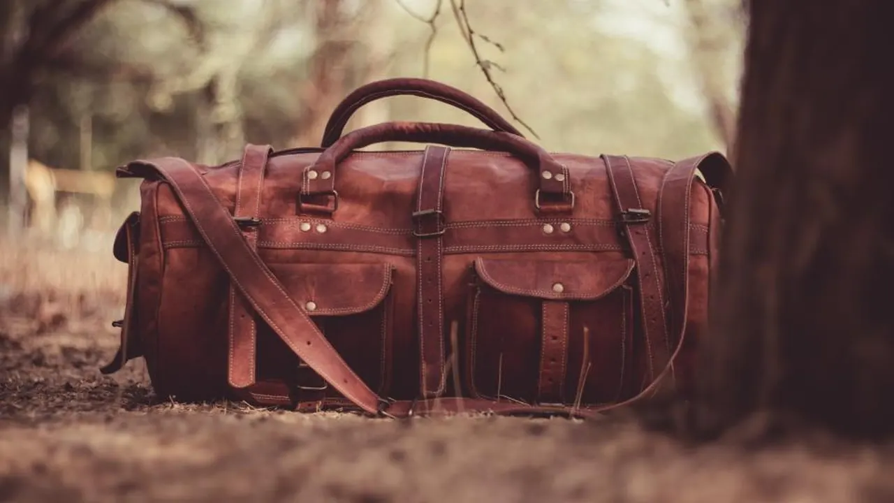 A brown leather holdall resting on a tree root in soft light