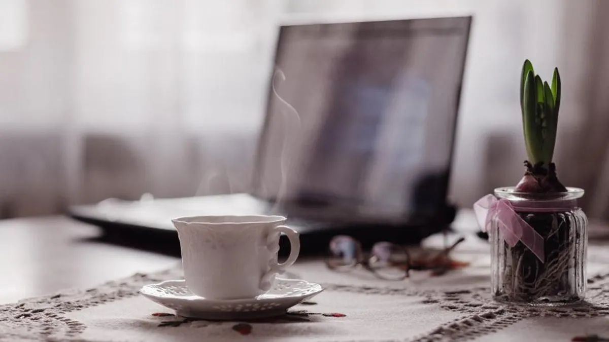A laptop and coffee cup on a table by a window