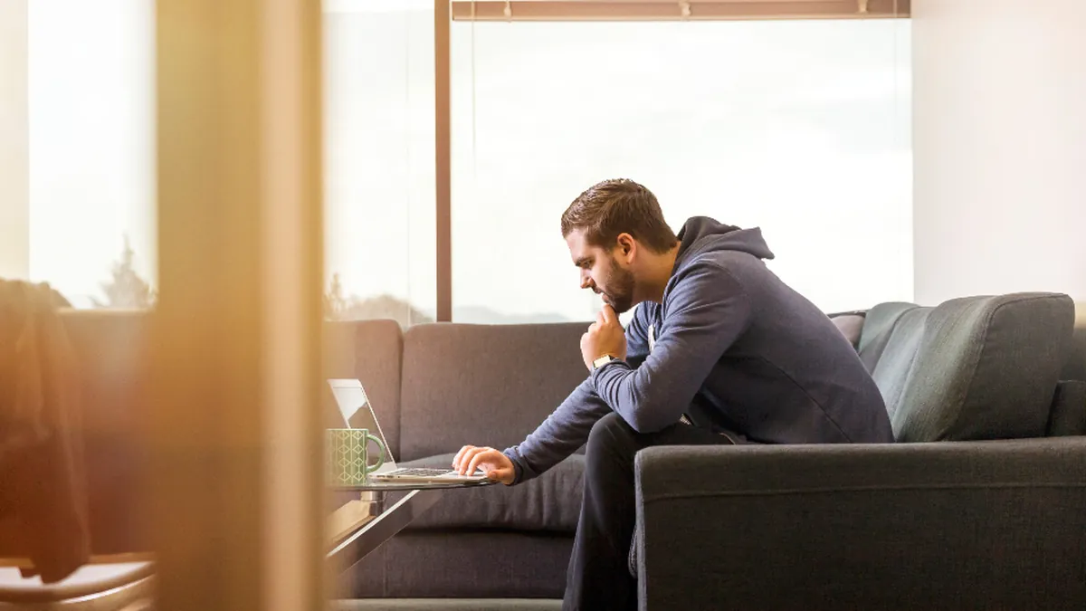 A man sitting on a sofa thinking while working on a laptop
