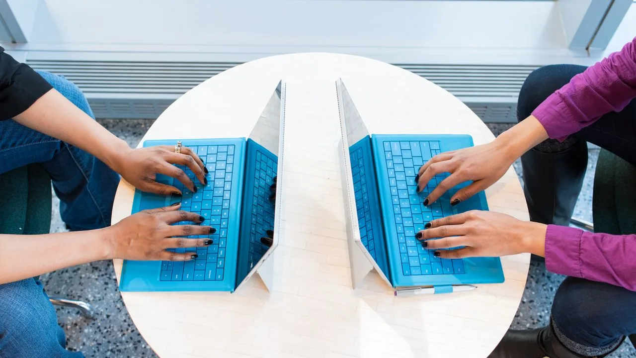 Two people working side by side on laptops at a shared desk