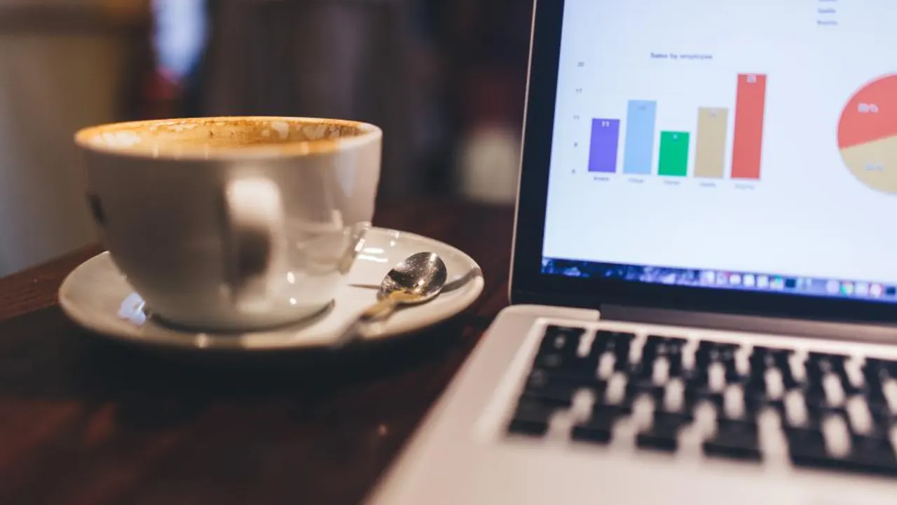 A cup of coffee beside a laptop showing colourful charts
