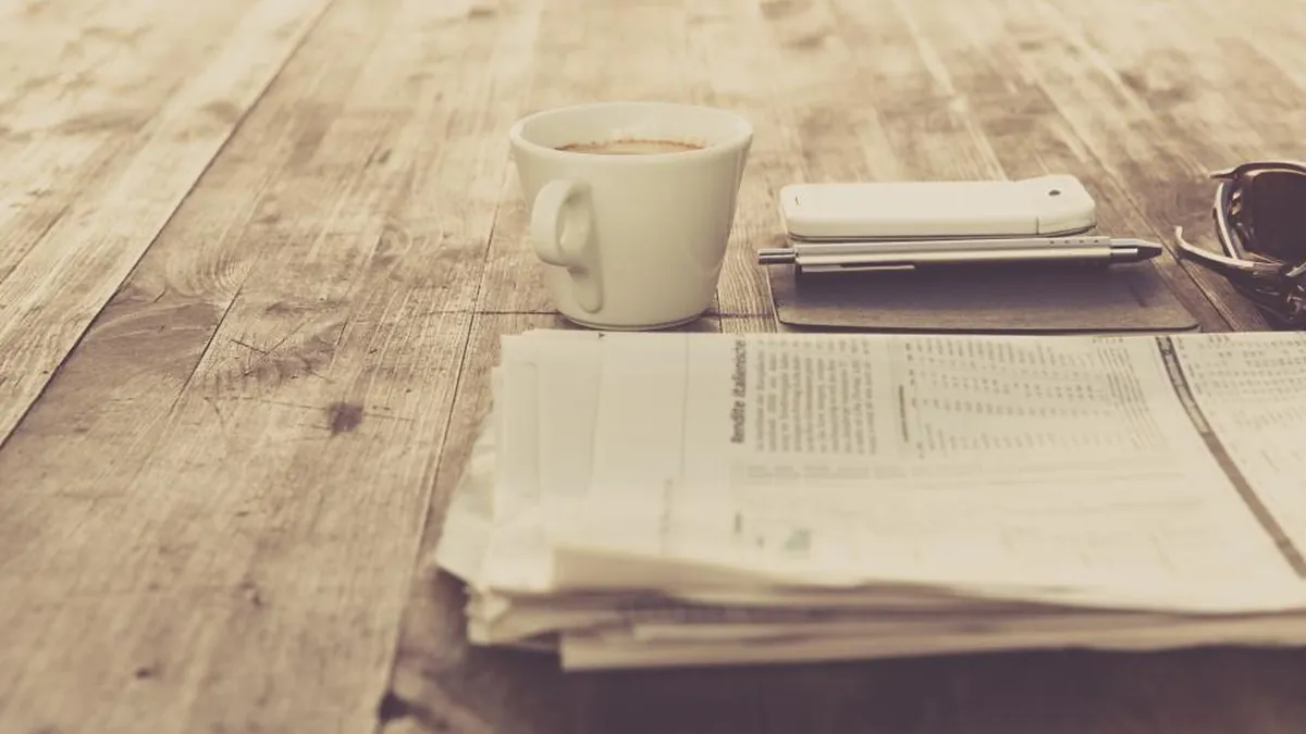 A cup of coffee, a phone and papers laid out on a wooden table