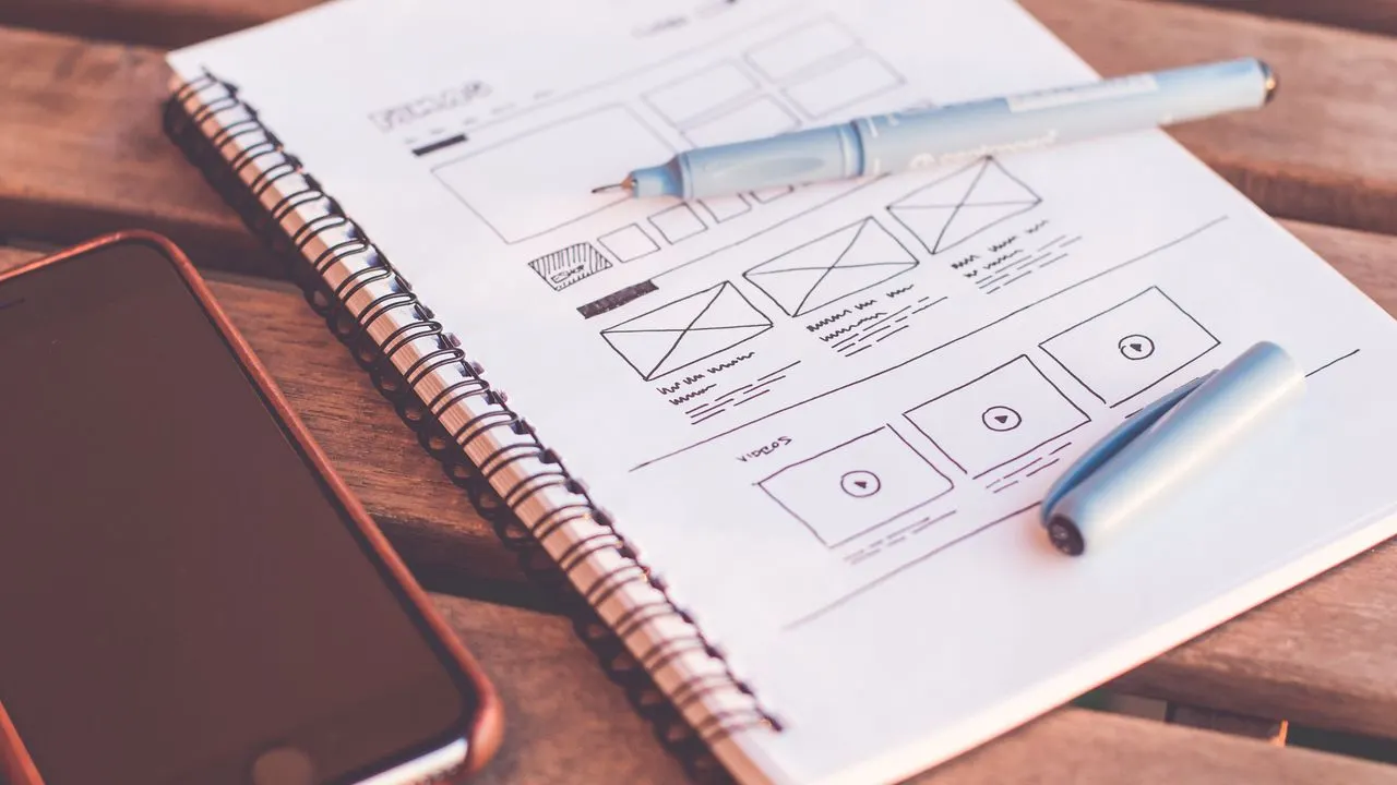 A notebook with website wireframe sketches beside a smartphone
