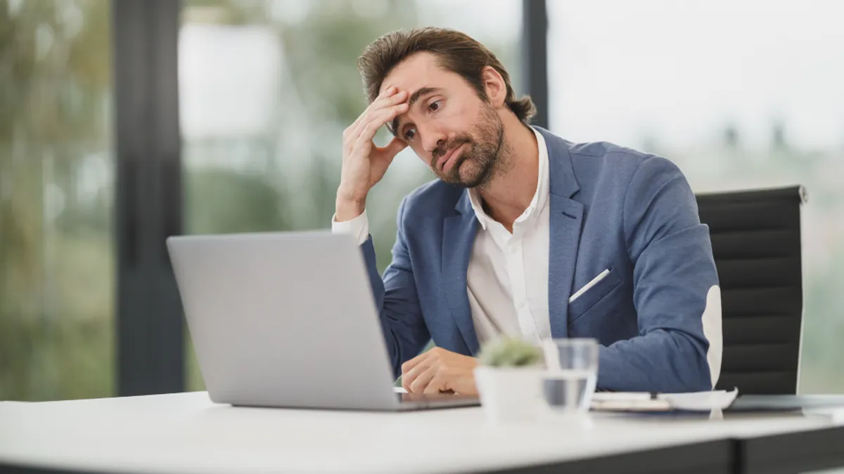 A frustrated businessman at a laptop holding his head